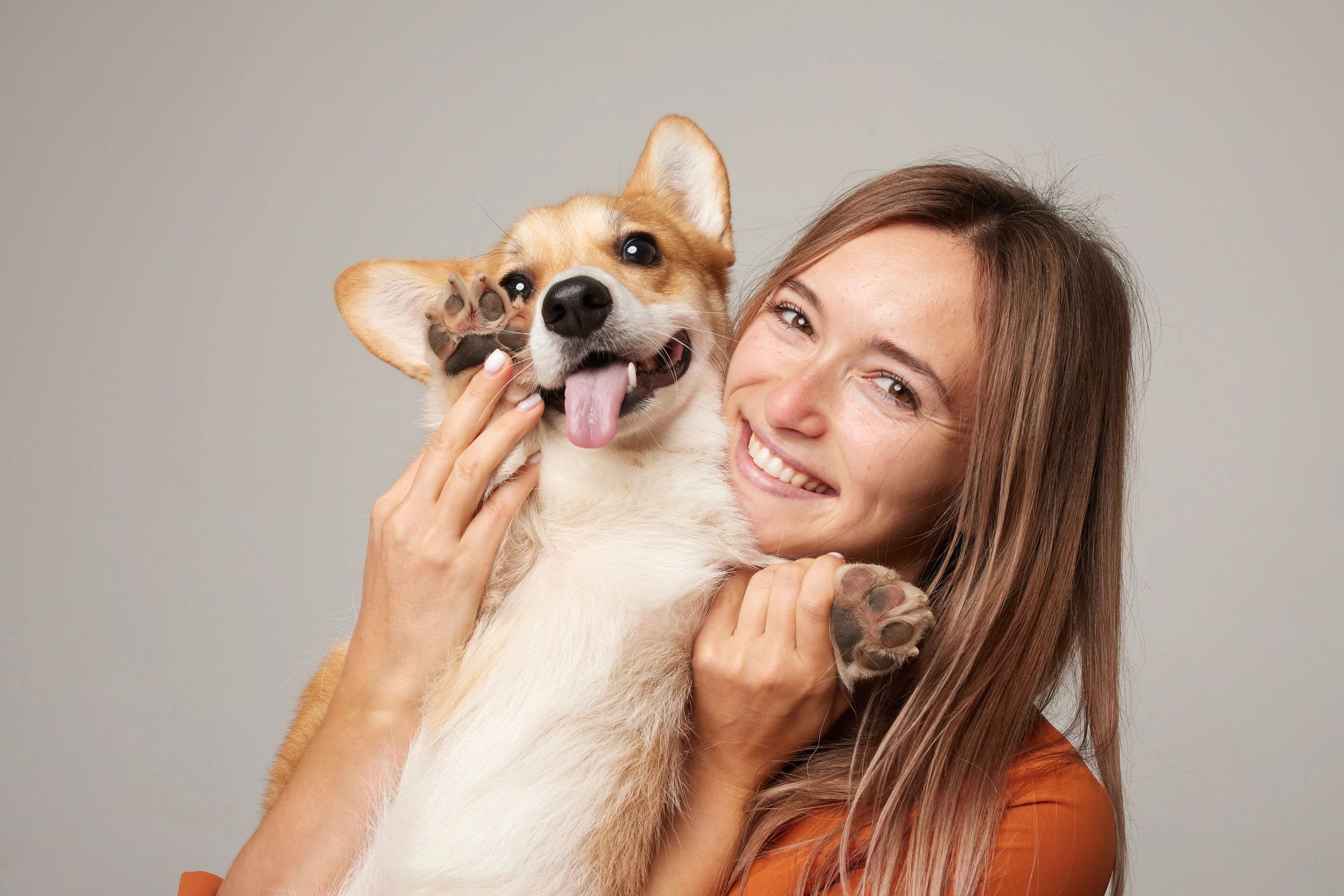 Woman hugging corgi on light background