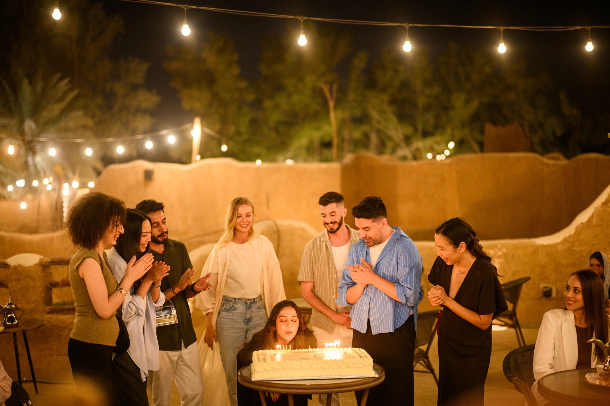 Friends celebrating around a birthday cake under string lights