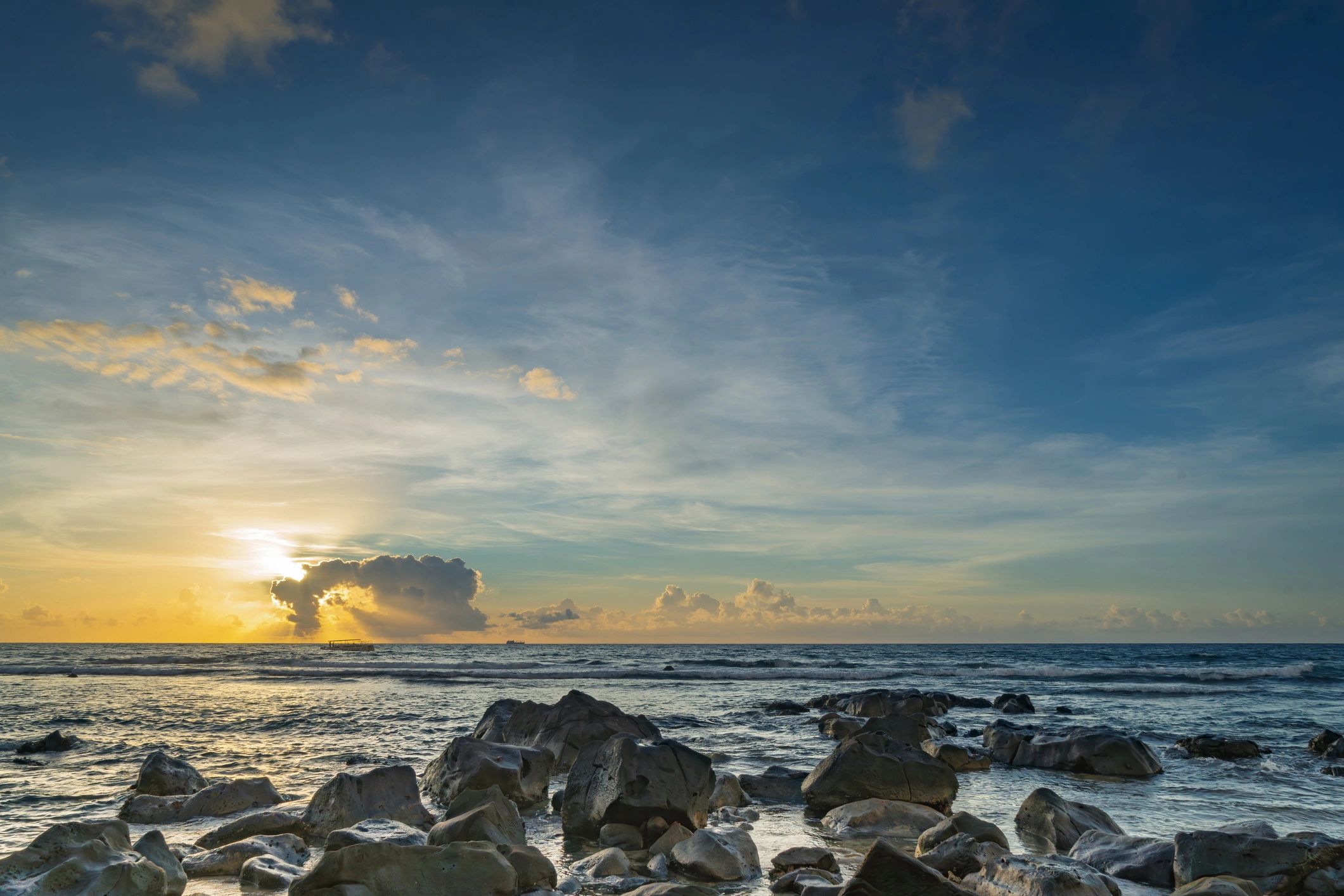 Rocky shoreline sunset with distant ship