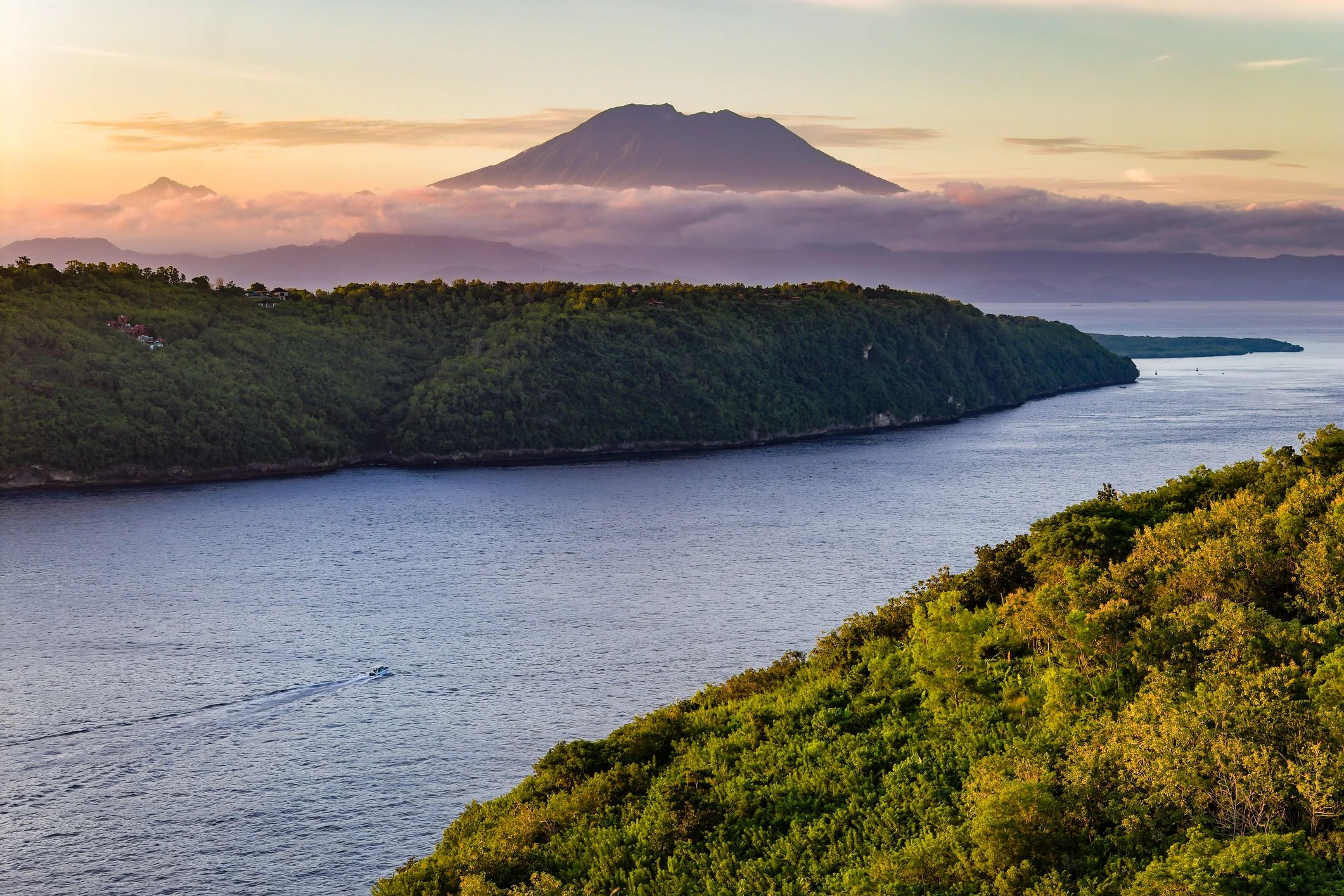 Coastal landscape with boat and distant volcano at sunset